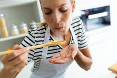 Alimento de cozimento e de sopro da jovem mulher saudável com a colher de madeira na cozinha em casa fotos de stock Alimento de cozimento e de sopro da jovem mulher saudável com a colher de madeira na cozinha em casa fotos de stock