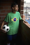 Allvarlig ung brasiliansk fotbollspelare som ut ser det Favela fönstret arkivfoto Allvarlig ung brasiliansk fotbollspelare som ut ser det Favela fönstret arkivfoto