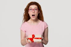 Amazed red-haired woman holding gift box looking at camera stock image Amazed red-haired woman holding gift box looking at camera stock image