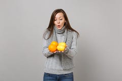 Amazed young woman in gray sweater, scarf holding, looking on lemons and oranges isolated on grey background. Healthy royalty free stock photo Amazed young woman in gray sweater, scarf holding, looking on lemons and oranges isolated on grey background. Healthy royalty free stock photo