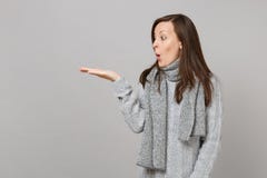 Amazed young woman in gray sweater, scarf looking, pointing hand aside on grey background, studio portrait stock image Amazed young woman in gray sweater, scarf looking, pointing hand aside on grey background, studio portrait stock image