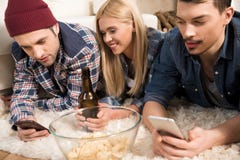 Amigos jovenes que mienten en la alfombra y que usan smartphones mientras que bebe la cerveza imagen de archivo libre de regalías Amigos jovenes que mienten en la alfombra y que usan smartphones mientras que bebe la cerveza imagen de archivo libre de regalías