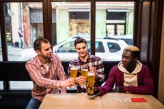 Amigos multirraciais felizes novos dos homens que bebem a cerveja e que falam no bar fotos de stock Amigos multirraciais felizes novos dos homens que bebem a cerveja e que falam no bar fotos de stock
