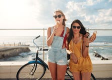 Amis féminins avec un vélo mangeant la crème glacée image stock Amis féminins avec un vélo mangeant la crème glacée image stock