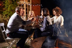 Amis mûrs appréciant le dîner extérieur autour de Firepit photographie stock Amis mûrs appréciant le dîner extérieur autour de Firepit photographie stock