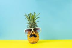 Ananas mûr jaune dans des lunettes de soleil avec le fond bleu jaune de moustache noire Visage drôle de fruit tropical Concept photographie stock Ananas mûr jaune dans des lunettes de soleil avec le fond bleu jaune de moustache noire Visage drôle de fruit tropical Concept photographie stock