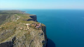 Ancient lighthouse up on the rock, located on the edge of green rocky mountain cliff and seascape breathtaking aerial drone point