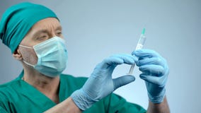 Anesthesiologist in face mask checking syringe for injection, operating theater stock image Anesthesiologist in face mask checking syringe for injection, operating theater stock image