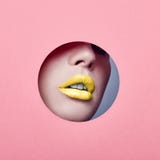Annonçant la couleur jaune lumineuse de belles lèvres dodues, la femme regarde en papier rose coloré par trou, salon de beauté Ma image stock Annonçant la couleur jaune lumineuse de belles lèvres dodues, la femme regarde en papier rose coloré par trou, salon de beauté Ma image stock