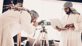 Araber som ser på teleskopet och rymmer bärbara datorn arkivfoto Araber som ser på teleskopet och rymmer bärbara datorn arkivfoto