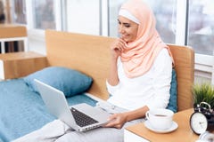An arabian woman is drinking tea and working on the computer while sitting on the bed. stock photo An arabian woman is drinking tea and working on the computer while sitting on the bed. stock photo
