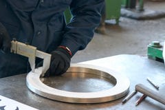 Arbetaren mäter detaljen, en skinande metallisk cirkel med en klämma på en funktionsduglig grön tabell i fabriken, seminariet fotografering för bildbyråer Arbetaren mäter detaljen, en skinande metallisk cirkel med en klämma på en funktionsduglig grön tabell i fabriken, seminariet fotografering för bildbyråer