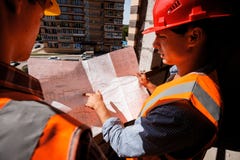 Architect and structural engineer dressed in shirts, orange work vests and helmets explore construction documentation on stock images Architect and structural engineer dressed in shirts, orange work vests and helmets explore construction documentation on stock images
