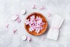 Aromatherapy, beauty and spa background with perfumed pink flowers water in wooden bowl and candles on stone table. Flat lay.