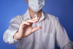 Arts in masker met een injectiespuit op de blauwe achtergrond stock afbeelding Arts in masker met een injectiespuit op de blauwe achtergrond stock afbeelding