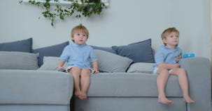 As crianças estão olhando a tevê Crianças pequenas que sentam-se nos desenhos animados de observação do sofá As crianças estão olhando a tevê Crianças pequenas que sentam-se nos desenhos animados de observação do sofá