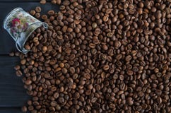 As grões perfumadas Roasted do café preto são dispersadas de uma cubeta do metal branco em uma tabela preta foto de stock royalty free As grões perfumadas Roasted do café preto são dispersadas de uma cubeta do metal branco em uma tabela preta foto de stock royalty free