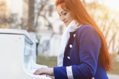 As mulheres caucasianos europeias com cabelo vermelho sorriem e jogam o piano no parque no por do sol A m?sica cl?ssica moderna e fotografia de stock As mulheres caucasianos europeias com cabelo vermelho sorriem e jogam o piano no parque no por do sol A m?sica cl?ssica moderna e fotografia de stock