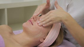 As mãos do cosmetologist untam a cara fêmea nova com creme de hidratação no salão de beleza luxuoso dos termas video estoque As mãos do cosmetologist untam a cara fêmea nova com creme de hidratação no salão de beleza luxuoso dos termas video estoque