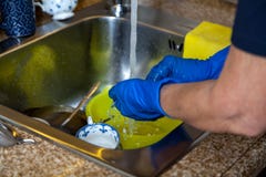 As mãos em luvas de borracha azuis lavam pratos no dissipador foto de stock As mãos em luvas de borracha azuis lavam pratos no dissipador foto de stock