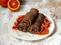 As panquecas finas do chocolate rolaram em um tubo com molho das laranjas pigmentadas em uma placa branca Pilha de crepes, blin d imagens de stock As panquecas finas do chocolate rolaram em um tubo com molho das laranjas pigmentadas em uma placa branca Pilha de crepes, blin d imagens de stock