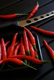 As vagens vermelhas dos pimentões e uma faca para o queijo e os vegetais encontram-se em uma superfície de madeira preta Luz do d fotos de stock royalty free As vagens vermelhas dos pimentões e uma faca para o queijo e os vegetais encontram-se em uma superfície de madeira preta Luz do d fotos de stock royalty free
