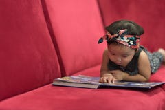 Asian baby toddler lying down on red sofa reading book stock photography Asian baby toddler lying down on red sofa reading book stock photography