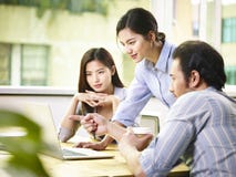 Asian business executives working together in office. A team of young asian corporate executives discussing business in office using laptop computer Asian business executives working together in office. A team of young asian corporate executives discussing business in office using laptop computer