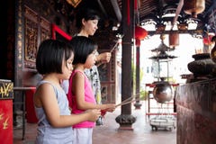 Asian Little Chinese Sisters And Mother Praying With Burning Incense Sticks Stock Image