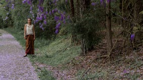 Asian woman in sarong walking on sidewalk covered with wisteria petals stock photo Asian woman in sarong walking on sidewalk covered with wisteria petals stock photo