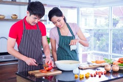 Asian young couple`s in apron, make cooking together. man are preparing to cut vegetables with knives. Woman mix salad dressing. stock photos Asian young couple`s in apron, make cooking together. man are preparing to cut vegetables with knives. Woman mix salad dressing. stock photos