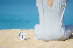 Asiatinnen in einem grauen Kleid, das neben dem weißen Wecker gesetzt auf den Sand sitzt Blaues Meer und Himmel als Hintergrund K lizenzfreie stockfotos Asiatinnen in einem grauen Kleid, das neben dem weißen Wecker gesetzt auf den Sand sitzt Blaues Meer und Himmel als Hintergrund K lizenzfreie stockfotos