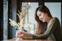 Asiatische Frau der Nahaufnahme, die ein Buch am hölzernen Gegenschreibtisch in der Kaffeestube mit Lächelngesicht in der glückli lizenzfreie stockbilder Asiatische Frau der Nahaufnahme, die ein Buch am hölzernen Gegenschreibtisch in der Kaffeestube mit Lächelngesicht in der glückli lizenzfreie stockbilder