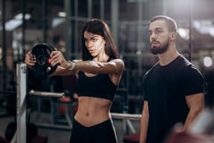 Athletic girl doing exercise for the muscles of the arms with weight in the gym under the supervision of a coach stock photo Athletic girl doing exercise for the muscles of the arms with weight in the gym under the supervision of a coach stock photo