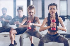 Athletic young people in sportswear with dumbbells squatting and exercising at the gym Royalty Free Stock Photos Athletic young people in sportswear with dumbbells squatting and exercising at the gym Royalty Free Stock Photos