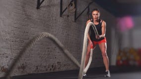 Athletische Frau aktiv in einer Turnhalle trainiert mit Kampf-Seilen während ihres Quereignungs-Trainings Langsame Bewegung stock video Athletische Frau aktiv in einer Turnhalle trainiert mit Kampf-Seilen während ihres Quereignungs-Trainings Langsame Bewegung stock video