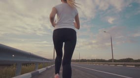 Atletiekklassen in de het plaatsen zon Een sportief meisje in een witte t-shirt, in heldere tennisschoenen en met lang haar loopt stock video Atletiekklassen in de het plaatsen zon Een sportief meisje in een witte t-shirt, in heldere tennisschoenen en met lang haar loopt stock video
