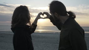 Atrakcyjni potomstwa dobierają się obsiadanie na plażowym dopatrywaniu zmierzch i robić kierowemu kształtowi z ich rękami w zwoln zdjęcie wideo Atrakcyjni potomstwa dobierają się obsiadanie na plażowym dopatrywaniu zmierzch i robić kierowemu kształtowi z ich rękami w zwoln zdjęcie wideo