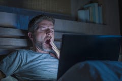 Atrakcyjny zmęczony i zaakcentowany workaholic mężczyzna pracuje nocny skołowanego na łóżkowy ruchliwie z laptopu ziewający czuci zdjęcie royalty free Atrakcyjny zmęczony i zaakcentowany workaholic mężczyzna pracuje nocny skołowanego na łóżkowy ruchliwie z laptopu ziewający czuci zdjęcie royalty free