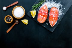 Att laga mat laxbiff från rå fisk på den svarta plattan med kryddor, rosmarin, citron och saltar på mörkt svart restaurangkök arkivbilder Att laga mat laxbiff från rå fisk på den svarta plattan med kryddor, rosmarin, citron och saltar på mörkt svart restaurangkök arkivbilder