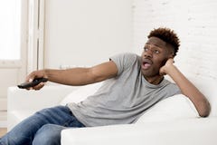 Attractive black african american man sitting at home sofa couch watching television stock images Attractive black african american man sitting at home sofa couch watching television stock images