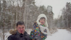 Attractive family having fun in a snow winter park. Cute little boy throws snowball. Father and son playing outside on stock video footage Attractive family having fun in a snow winter park. Cute little boy throws snowball. Father and son playing outside on stock video footage