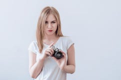 Attractive girl holding a vintage camera in her hands. Confusedly looks