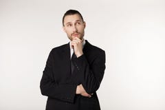 Attractive guy, teacher with stylish hair and beard in black suit holding his chin and thoughtfully looking aside royalty free stock photography Attractive guy, teacher with stylish hair and beard in black suit holding his chin and thoughtfully looking aside royalty free stock photography