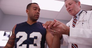 Attractive male sports athlete with mid aged male doctor examining injury royalty free stock photography Attractive male sports athlete with mid aged male doctor examining injury royalty free stock photography
