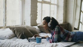 Attractive mixed race girl listen to music while surfing social media on laptop lying on bed