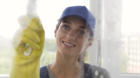 Happy young woman of the cleaning service spraying detergent and cleaning the window with little mop