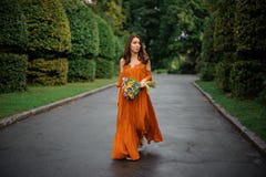 Attractive woman in orange dress walking on the road with bouquet of flowers. Attractive woman in long orange dress walking on the road with bouquet of flowers Stock Images Attractive woman in orange dress walking on the road with bouquet of flowers. Attractive woman in long orange dress walking on the road with bouquet of flowers Stock Images