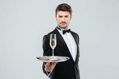 Attractive young butler in tuxedo offers you glass of champagne. Attractive young butler in tuxedo with bow tie offers you glass of champagne royalty free stock photography Attractive young butler in tuxedo offers you glass of champagne. Attractive young butler in tuxedo with bow tie offers you glass of champagne royalty free stock photography