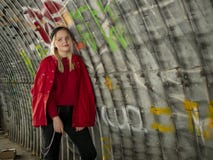 Attractive young hipster girl in knitted hat and red jacket is standing under a bridge against the background of a wall with stock image Attractive young hipster girl in knitted hat and red jacket is standing under a bridge against the background of a wall with stock image